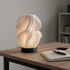 Modern table lamp with wavy design on a wooden table next to a notebook and pen.