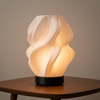Decorative table lamp with wavy design on a wooden table against a neutral background